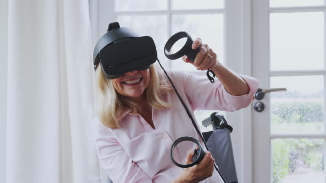Reife-behinderte-Frau-im-Rollstuhl-zu-Hause-mit-Virtual-Reality-Headset-Gaming-Holding-Controller