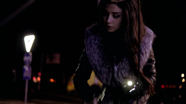 Young-brunette-woman-with-long-hair-is-looking-under-the-hood-using-her-smartphone-as-a-flashlight