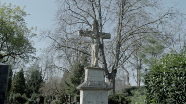 Old-tombstone-with-Jesus-cross-on-a-sunny-spring-day.-Tilt-from-tombstone-to-sky.-4K-in-SLOG3.-Long-shot.