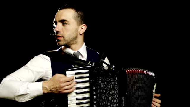 A-fashionable-musician-in-a-white-shirt-plays-the-accordion-in-the-studio-on-a-black-background.