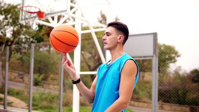 Retrato-de-un-jugador-de-baloncesto-que-hace-girar-una-pelota-de-baloncesto-en-el-patio-de-la-calle.-Tiro-de-cámara-lenta