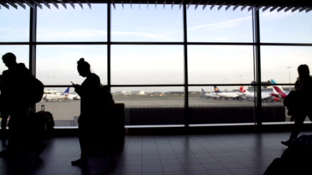 Silhouettes-of-tourists-walking-by-huge-terminal-window,-passengers-at-airport