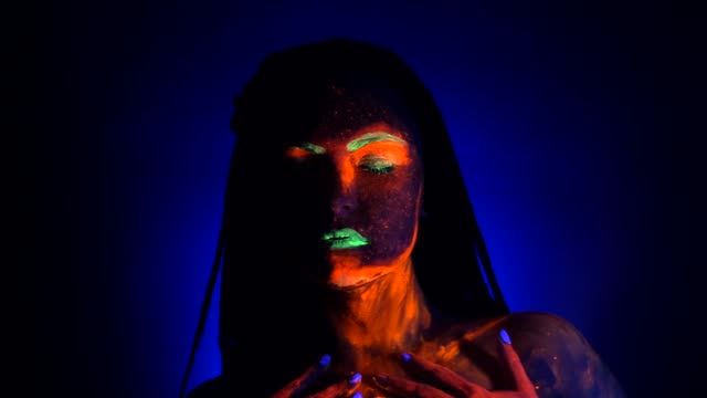 Girl-sexy-smears-and-rubs-fluorescent-paint-on-her-body.-Dye-glowing-under-UV-black-light.-Woman-with-braids-in-neon-light.-Night-club,-party,-halloween-psychedelic-concepts
