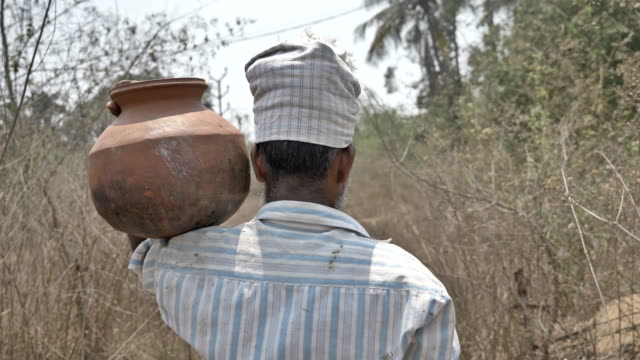 A-male-farmer-walking-while-carrying-a-earthen-pot-filled-with-water-on-his-shoulder