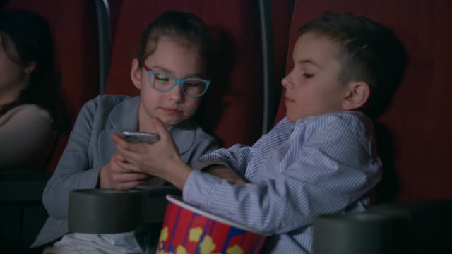 Kinder-essen-Popcorn-im-Kino.-Kinder-mit-Handy-im-Kino