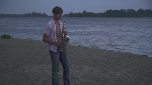 Chico-joven-guapo-es-jugar-el-saxophone-en-la-orilla-del-río