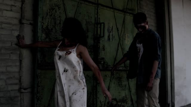 Zwei-Zombies-gehen-mit-einem-verlassenen-Haus-auf-den-Hintergrund.-Brünettes-Girl-mit-Verwundeten-Gesicht-und-blutigen-weißen-Kleid-und-verletzten-männlichen-Zombie-walking-im-freien