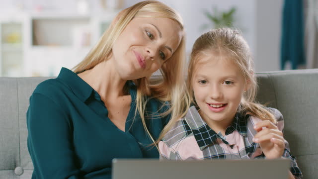 Hermosa-joven-madre-y-su-linda-pequeña-portátil-de-uso-hija-mientras-estaba-sentado-en-un-sofá-en-casa.-Familia-pasar-tiempo-junto-viendo-Videos-y-dibujos-animados-en-computadora.