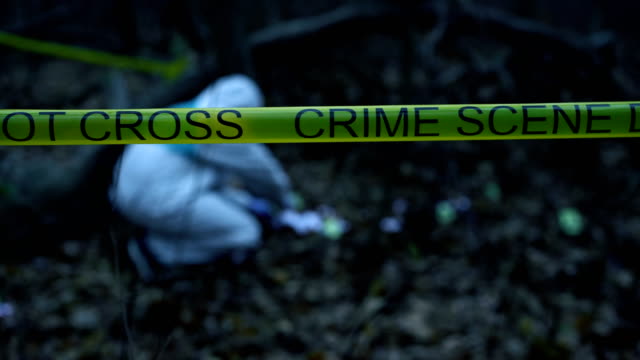 Yellow-crime-scene-tape-in-forest,-forensic-expert-collecting-evidence-at-site