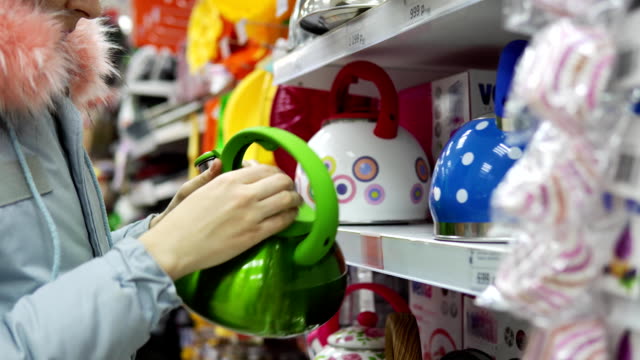 A-young-woman-chooses-a-green-steel-kettle-in-the-supermarket.