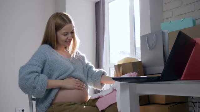 Internet-gekauft-moderne-Schwangerschaft,-Mutterschaft-Frau-mit-nackten-Bauch-unter-Berücksichtigung-neuer-Kleidung-für-zukünftiges-Kind-sitzt-vor-dem-computer