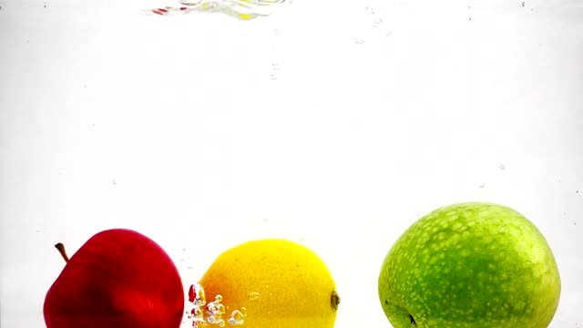 The-apple,-lemon-and-orange-falling-in-water-with-bubbles-in-slow-motion.-Fruits-on-isolated-a-white-background.