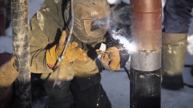 Worker-produces-pipe-welding-on-the-street.-In-winter,-at-low-temperatures,-it-is-difficult-to-mount-the-pipe-wire