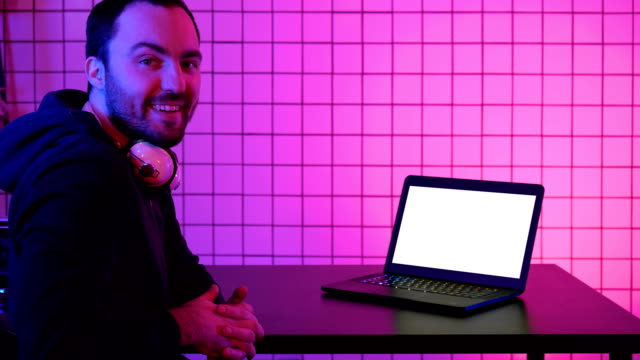 A-young-cheerful-gamer-smiling-to-the-camera-and-looking-at-laptop.-White-Display