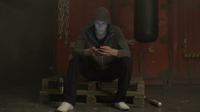 Grim-man-in-hoodie-text-messaging-on-cellphone