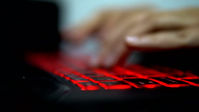 Teenage-Hacker-Girl-greift-Unternehmensserver-in-Dunkelheit-an,-tippen-auf-Red-Lit-Laptop-Keyboard.-Raum-ist-dunkel
