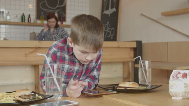 Kleine-Junge-spielen-am-Telefon,-während-sie-im-Café-essen