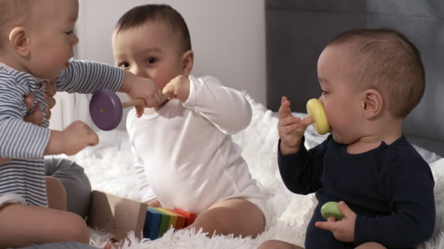 Asiatische-Baby-Triplets-sitzen-zusammen-im-Schlafzimmer-und-spielen-mit-Spielzeug