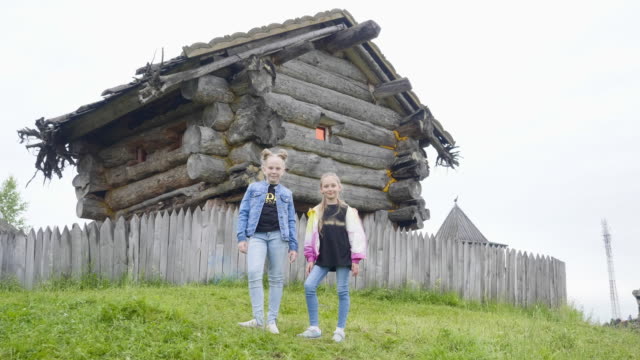 Zwei-Mädchen-Teenager-stehen-auf-grünem-Rasen-auf-rotierenden-Märchenhaus.-Teenager-Mädchen-posiert-auf-Holzhaus-der-alten-Hexe-im-Märchendorf