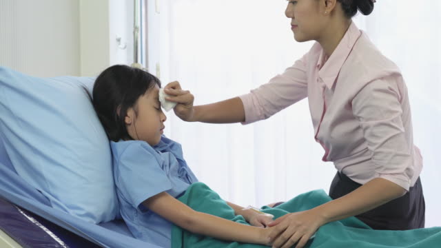 Madre-asiática-frotar-la-niña-paciente-del-cuerpo-para-reducir-la-temperatura-y-el-examen-físico-en-el-hospital.-Concepto-de-familia,-medicina,-salud-y-tecnología.