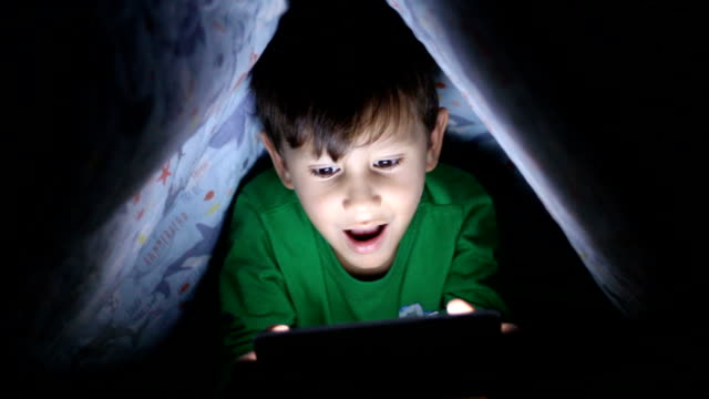 Little-boy-reading-book-on-digital-tablet-at-night