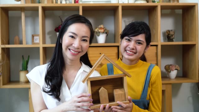 Positive-Asian-women-carrying-wooden-symbolic-miniature-house