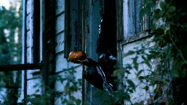 Halloween-make-up.-A-woman-sitting-in-doorway-of-house-and-holding-a-pumpkin.-4K