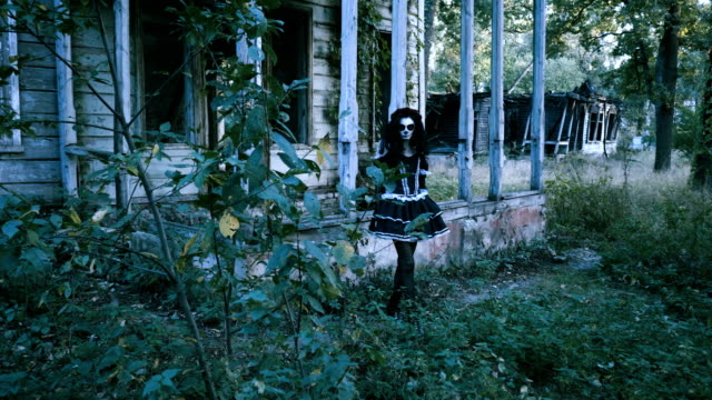 Una-mujer-con-maquillaje-de-esqueleto-para-Halloween-yendo-a-lo-largo-de-la-casa-de-madera.-4K