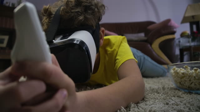 Close-up-portrait-of-teenage-Caucasian-boy-laying-on-the-floor-wearing-VR-headset-and-holding-remote-control.-Child-playing-virtual-reality-game.-Generation-Z,-gaming.-Cinema-4k-ProRes-HQ.
