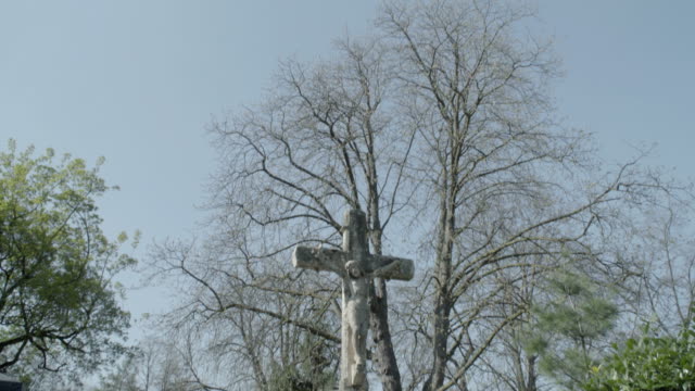 Old-tombstone-with-Jesus-cross-on-a-sunny-spring-day.-Tilt-from-sky-to-tombstone.-4K-in-SLOG3.-Long-shot.