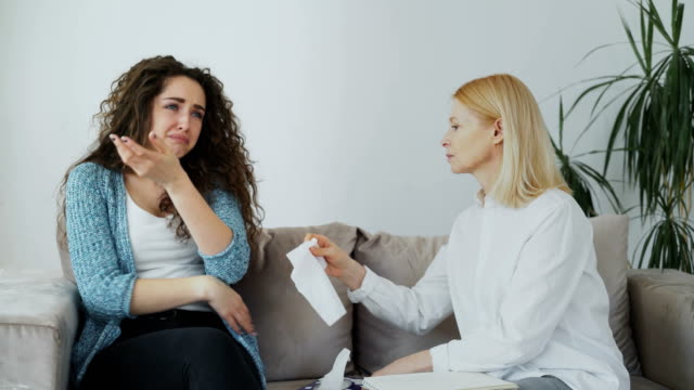Llorando-tensionó-mujer-conversar-con-profesional-psicólogo-femenina-que-le-da-su-pañuelo-de-papel-para-enjugando-sus-lágrimas