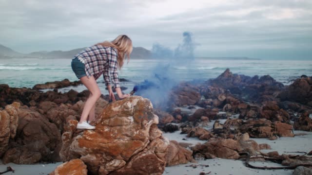Frau-mit-Rauchgranate-auf-den-Felsen-am-Strand
