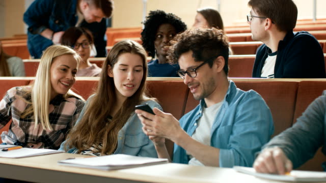 Männliche-Schüler-Aktien-Handy-Bildschirm-mit-anderen-Studenten,-sie-Lächeln.-Scherz-in-der-Universität-Klasse.