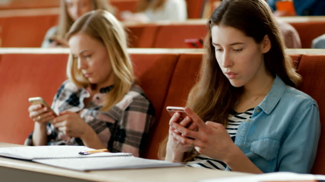 Múltiples-grupos-étnicos-de-estudiantes-utilizando-teléfonos-inteligentes-durante-la-Conferencia.-Jóvenes-personas-usando-las-redes-sociales-mientras-que-estudiar-en-la-Universidad.