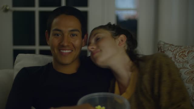 Una-joven-pareja-viendo-la-televisión-y-comiendo-palomitas-de-maíz-juntos,-beso-en-la-mejilla