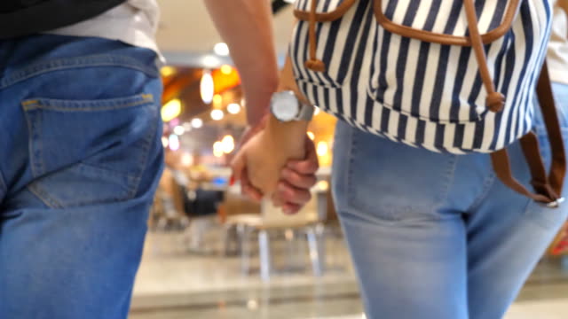 Young-couple-holding-hands-of-each-other-and-walking-at-terminal-of-airport.-Man-and-woman-taking-arms-and-stepping-during-trip.-Symbol-of-love-and-devotion.-Close-up-Rear-back-view