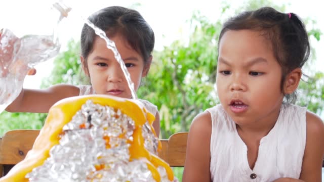 Dos-niñas-asiáticas-hacen-el-experimento-de-volcán-de-bicarbonato-de-sodio-y-vinagre-en-la-mesa-en-su-casa,-lenta-en-100-fps