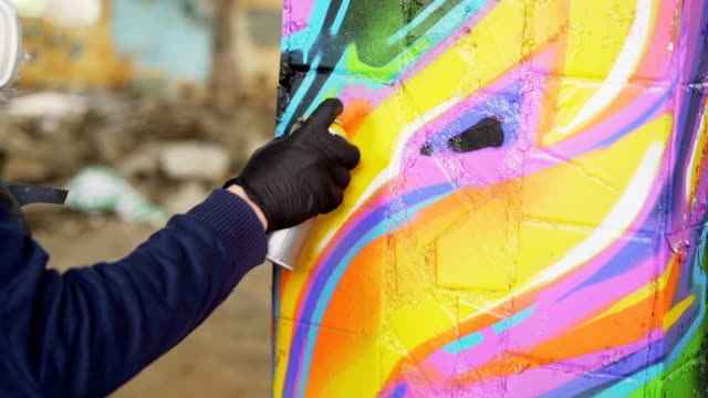 Nahaufnahme-der-männlichen-hand-in-Leder-Handschuh-mit-Sprühfarbe-und-Malerei-Graffiti-auf-alte-Säule-in-verlassenen-Gebäude.-Moderne-Kunst,-abstrakte-Bilder-und-Menschen-Konzept.