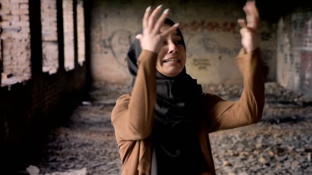 Young-muslim-woman-in-hijab-screaming-at-armed-soldier,-standing-in-abandoned-building,-terrorism-concept