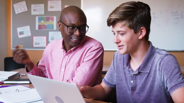 High-School-Lehrer-geben-männlichen-Studenten-mit-Laptop-Einzelunterricht-am-Schreibtisch