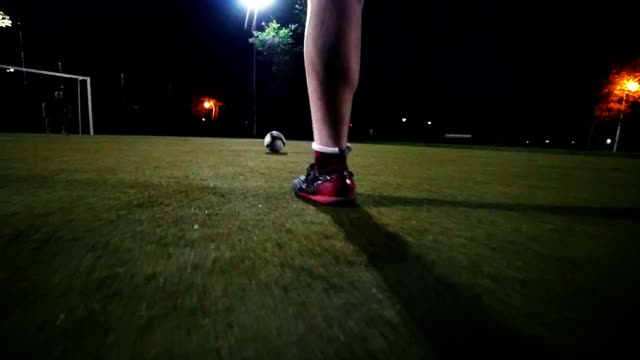 Player-in-black-and-red-sneakers-runs-up-to-the-ball-and-makes-a-kick-towards-the-goal,-but-the-goalkeeper-beats-the-ball,-green-grass,-night-shooting