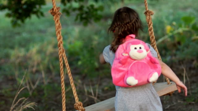 A-little-girl-with-a-backpack-on-her-back-came-to-ride-one-on-a-swing.-Summer-holidays