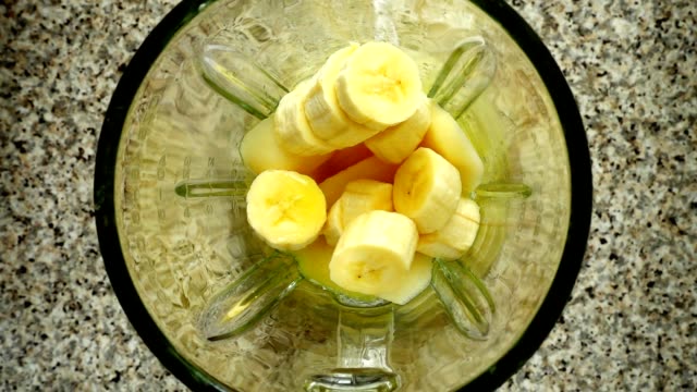 Pieces-of-apples-fall-in-a-blender-bowl-on-pieces-of-bananas.-Slow-motion.	Shooting-in-kitchen.-Top-view.