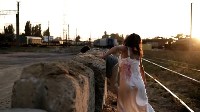 Picture-of-creepy-male-and-female-ghost-or-zombie-walking-with-wounded-face.-Male-zombie-climbing-on-blocks-on-the-ground.-Industrial,-abandoned-town,-raiways-around
