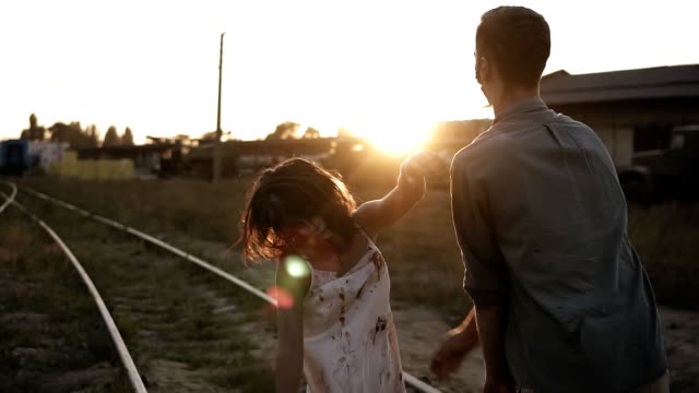 Halloween-horror-filming-concept.-Picture-of-creepy-male-and-female-zombies-outdoors,-standing-on-the-railway.-Abandoned-town-and-sun-shines-on-the-background