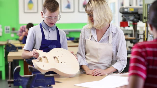 Mujer-profesora-ayuda-hombre-alta-escuela-estudiante-edificio-guitarra-lección-de-carpintería