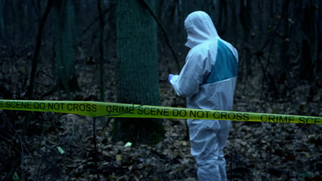 Forensic-analyst-in-white-protective-gear-working-with-evidence-at-crime-scene