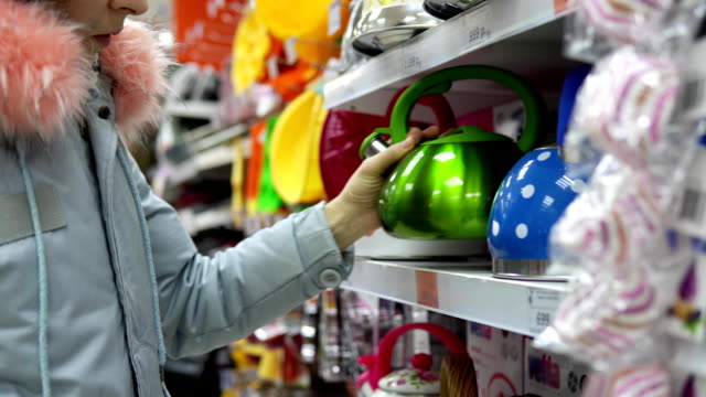 A-young-woman-chooses-a-green-steel-kettle-in-the-supermarket.