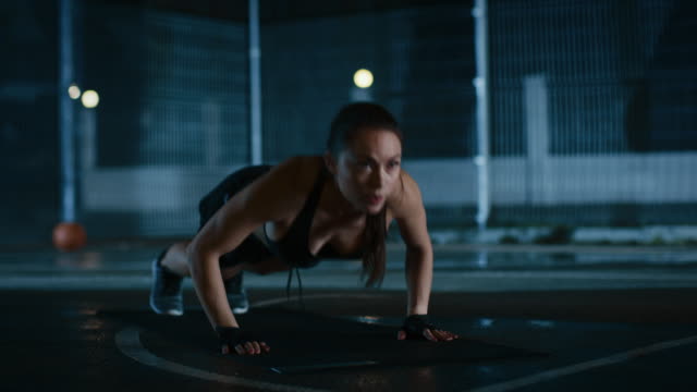 Beautiful-Sporty-Fitness-Girl-Doing-Push-Up-Exercises.-She-is-Doing-a-Workout-in-a-Fenced-Outdoor-Basketball-Court.-Night-Footage-After-Rain-in-a-Residential-Neighborhood-Area.