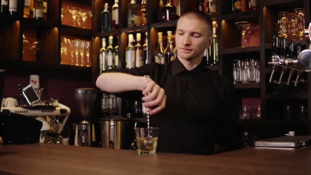 Joven-barman-en-la-barra-interior-vertiendo-whisky-en-cristal-y-trayendo-para-los-visitantes